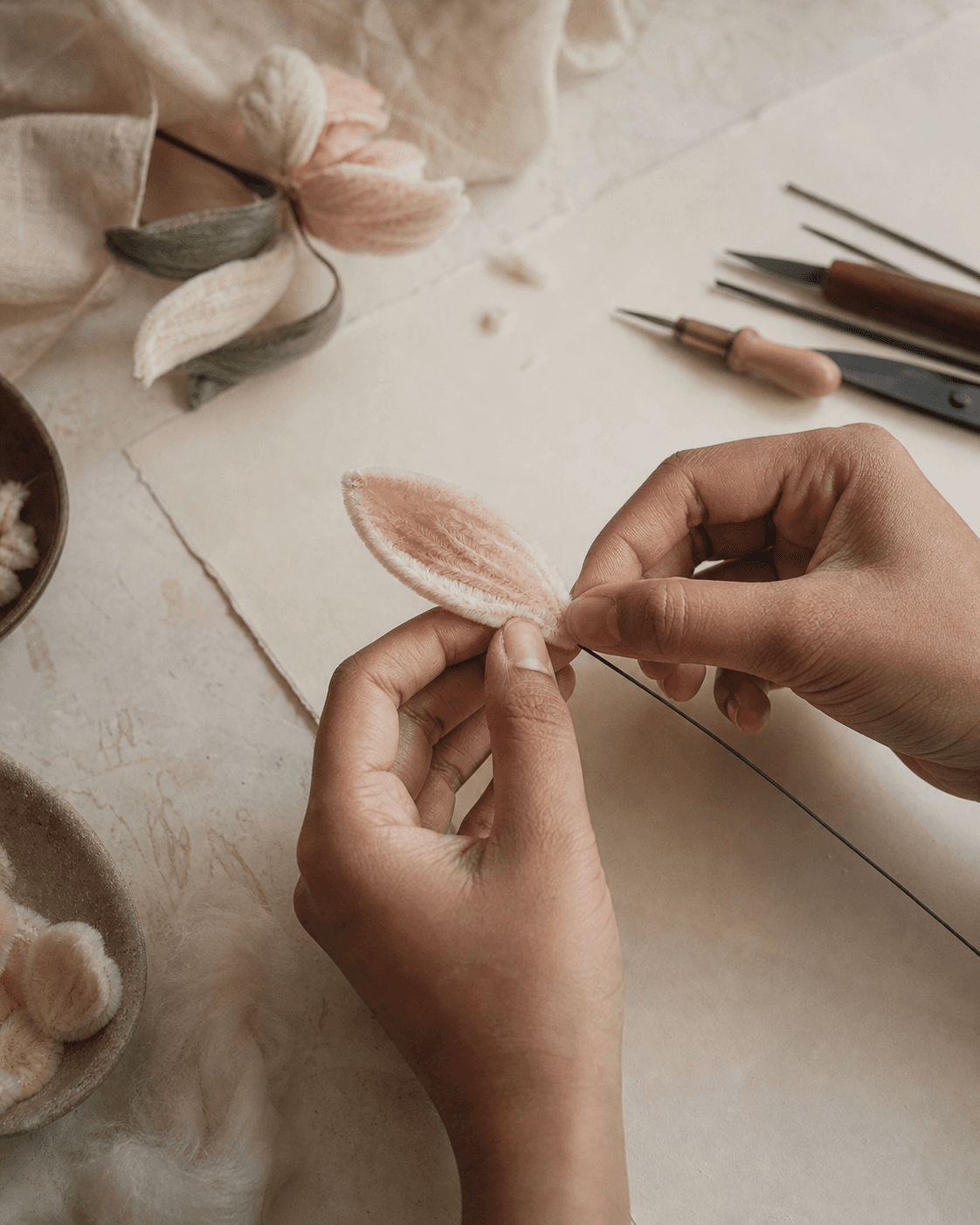 Hands shaping a soft fibre petal around a wire stem at the studio workbench.